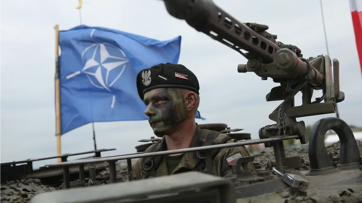 Солдат Войска Польского сидит в танке, а позади него развевается флаг НАТО во время военных учений в 2015 году в Жагани, Польша. Фото: Шон Гэллап/Getty Images